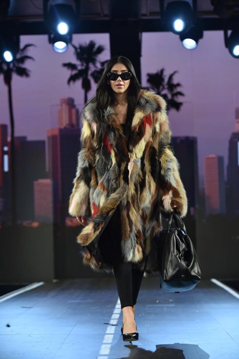 Model walking the Bugatti Runway 7 show at NYFW wearing a multi-tonal oversized faux fur coat with black sunglasses and a large leather weekender bag.