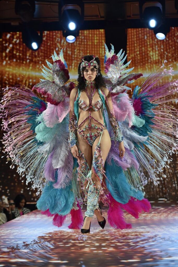 New York Fashion Week FW26 runway look featuring oversized carnival feather wings and cobalt blue sculptural lingerie set
